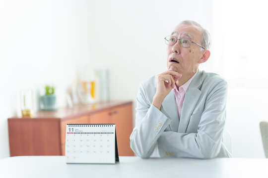 カレンダーの前で困った表情の高齢者の男性