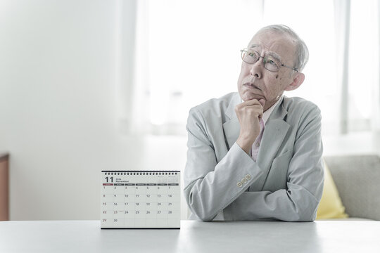 カレンダーの前で困った表情の高齢者の男性
