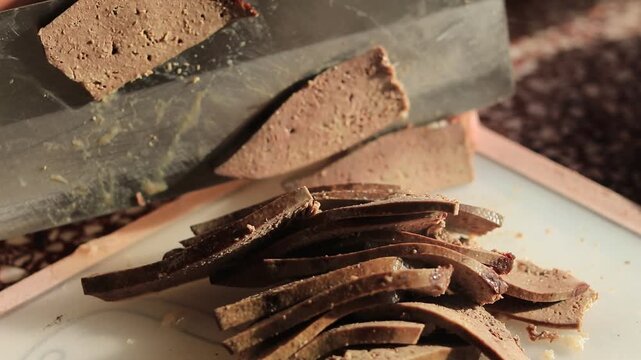 Close up of a home cook using a sharp knife to slice freshly boiled pork liver on a chopping board.