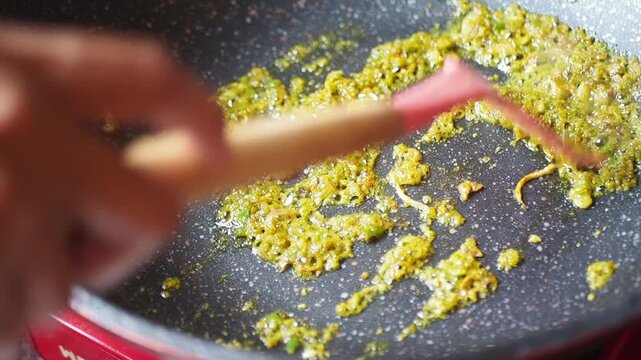 Close-up shot of curry paste being fried in a pan with a spatula, cooking food in kitchen