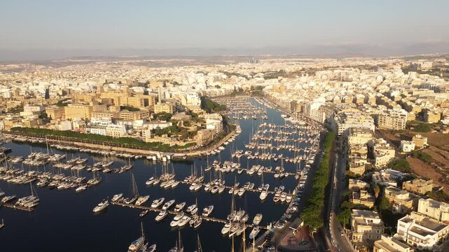 Aerial view of rows of yachts moored in the marina surrounded by urban buildings and rooftops under a clear sky in Ta' Xbiex, Eastern Region, Malta.