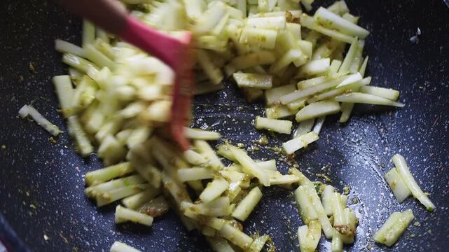 Close-up of julienned vegetables being stir-fried in a wok with spices and oil, using a pink spatula for mixing.