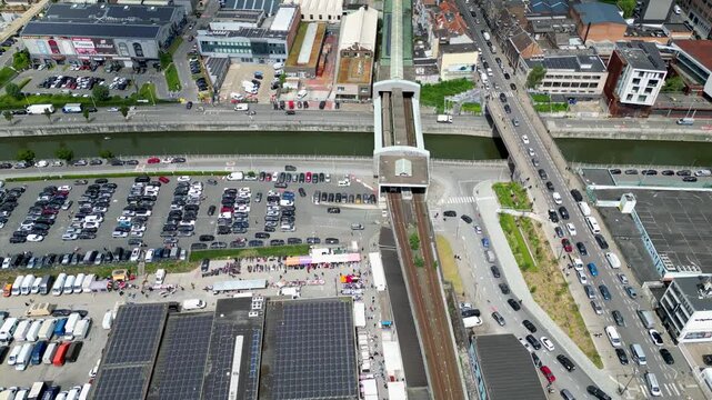 Aerial view of a busy urban area with a large parking lot, solar-paneled rooftops, and a railway line passing through the city of Anderlecht, Brussels, Belgium.