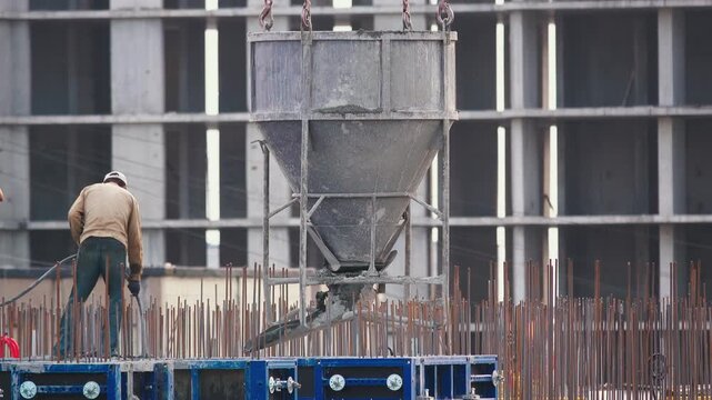 Construction Worker Operating Concrete Vibrator Hose on High Rise Building Site with Empty Skip Hanging Above | Static Telephoto Shot | Industrial Process