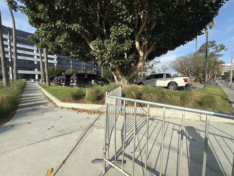 Manhattan Beach, United States - 14 June 2026: View of the westdrift Manhattan Beach hotel grounds with metal barricades, parked vehicles, and a large tree on a sunny day.