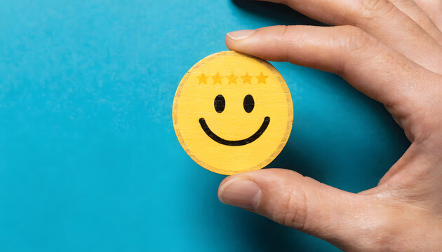 Closeup of a hand holding a yellow wooden circle with a smiling face and five stars icon, representing customer satisfaction and feedback