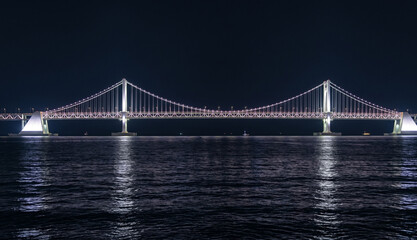 Fototapeta premium Illuminated suspension bridge over the dark sea at night