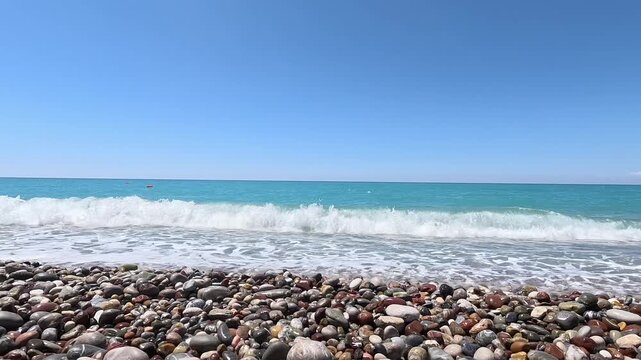 Wide scenic view of turquoise sea waves washing pebble beach under clear blue sky. Calm summer coastline, travel, vacation, nature and seaside relaxation concept.