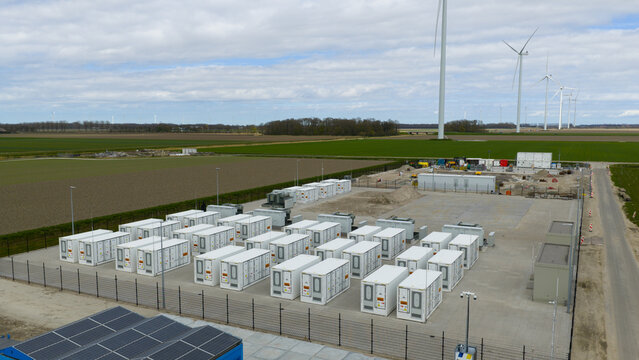 Dronten, Netherlands - 04 April 2026: Aerial view of a battery energy storage system with rows of white containers near wind turbines and solar panels in a flat rural landscape.