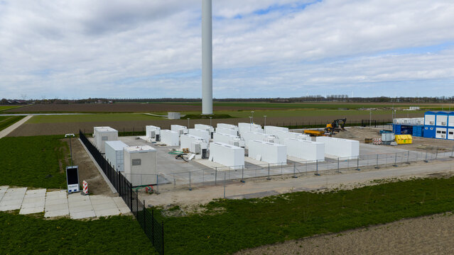 Dronten, Netherlands - 04 April 2026: Aerial view of a battery energy storage system facility with white containers and a wind turbine base in the flat landscape of Flevoland.