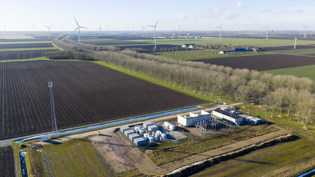 Zeewolde, Netherlands - 14 January 2026: Aerial view of an electrical substation and vast agricultural fields with wind turbines under a clear sky.