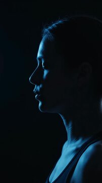 Silhouette of young woman illuminated by cool blue light in the dark. Vertical video