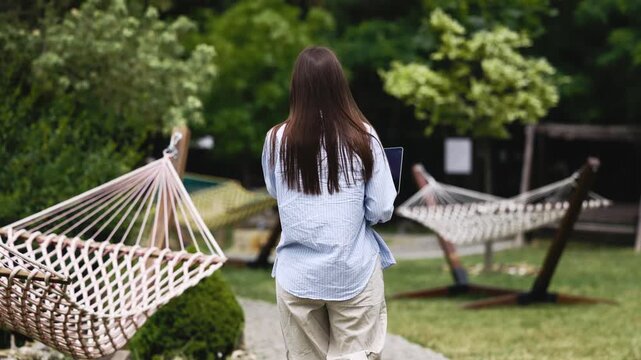 Female freelancer multitasking with laptop and smartphone during a business call in a garden setting. Concept remote work, communication and flexibility.
