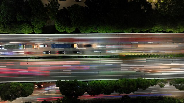 Cilandak, Indonesia - 10 April 2026: Aerial view of the Lebak Bulus highway at night with long exposure light trails from moving vehicles and lush green trees lining the road.