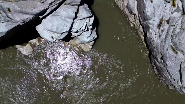 Top Down Aerial View of Muddy River and Smooth White Rocks in Ecuador, Tropical Canyon Geology, Sunlit Water Surface and Natural Erosion Texture