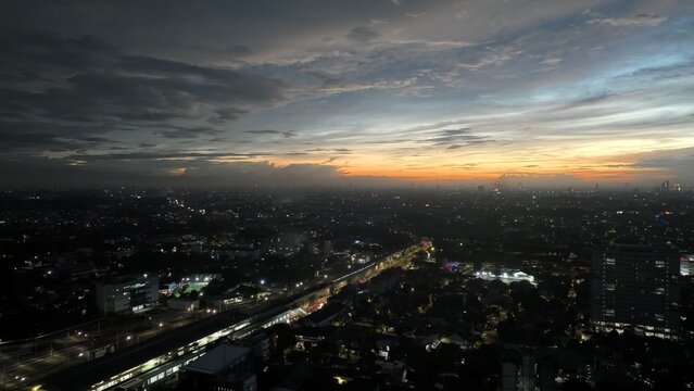 Cilandak, Indonesia - 10 April 2026: Aerial view of the Lebak Bulus area at dusk with the MRT station illuminated against a dramatic sunset sky and city lights.
