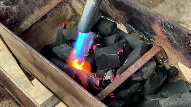 Using a gas torch to quickly ignite charcoal in a grill, creating a glowing red flame perfect for outdoor cooking.