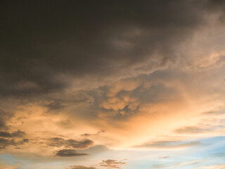 Obraz premium Sunset sky was beautiful, with thick, dark orange and golden clouds near the horizon and dark, warm-toned clouds turning cool blue at the bottom.