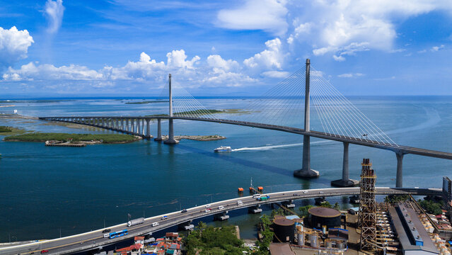 Cebu City, Philippines - 12 June 2026: Aerial view of the Cebu-Cordova Link Expressway bridge spanning across the sea with a boat passing underneath and white clouds in a blue sky.