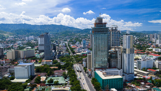 Cebu City, Philippines - 12 June 2026: Aerial view of modern skyscrapers and urban skyline with lush green mountains in the background under a blue sky with white clouds.