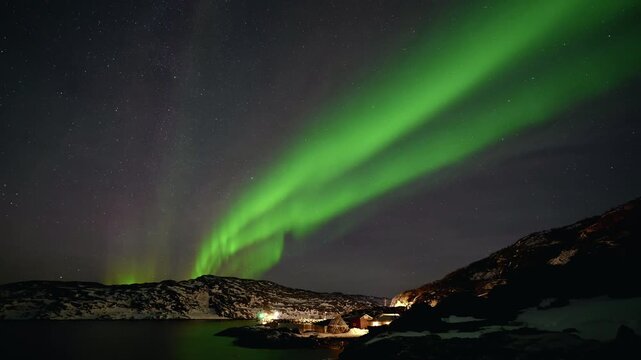 Green aurora arching over an Arctic town beneath a dark winter sky, powerful ribbon pillars
