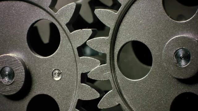 A cinematic close-up of interlocking metal cogs and gears rotating slowly within an industrial machine. The smooth mechanical movement highlights engineering precision, manufacturing processes, and th