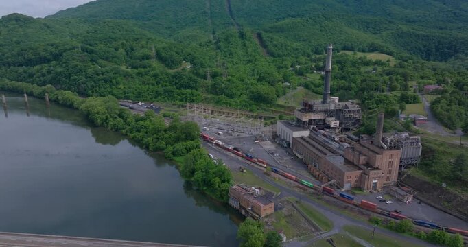Closed coal-fired power facility near river crossing and rail network, drone orbit ascend left