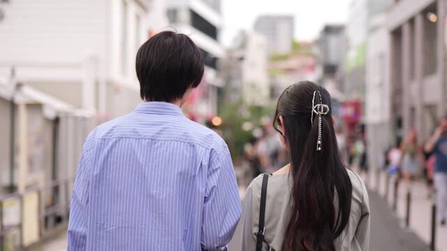 原宿のショッピングストリートを話しながら歩くカップルの後ろ姿のフォローショット