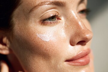 Fototapeta premium Radiant Skin Texture: A close-up profile shot of a woman's face, showcasing her skin's natural texture with a subtle application of cream, illuminated by soft sunlight.