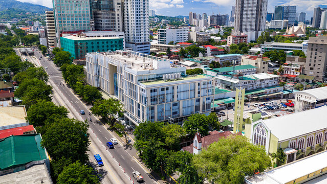 Cebu City, Philippines - 12 June 2026: Aerial view of modern urban buildings, a busy city street with vehicles, and lush green trees under a clear blue sky in Cebu City.