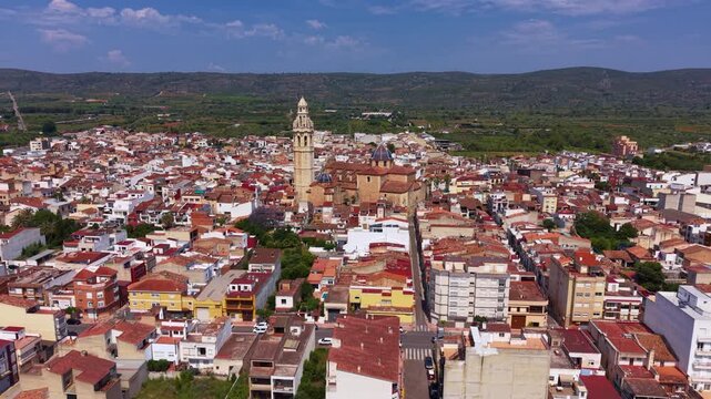 Parroquia de Sant Joan Baptista in Alcala de Xivert, Spain Valencian Baroque church with ornate octagonal bell tower and blue ceramic domes rising above terracotta rooftops with green hills beyond