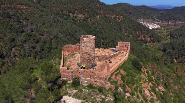 Castell de Benali ruins atop a forested hill in Sierra de Espadan national park, Spain, featuring a round stone tower within ancient walls surrounded by green pine forest