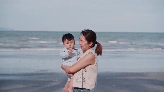 Young mother holding her adorable baby boy travel on the beach at sunny day.