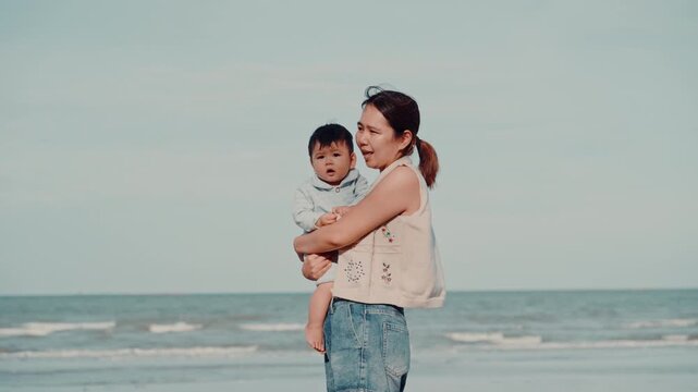 Young mother holding her adorable baby boy travel on the beach at sunny day.