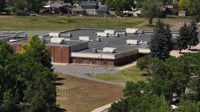 Aerial of school campus and sports fields in Littleton Colorado summer day with single story brick building and grassy fields