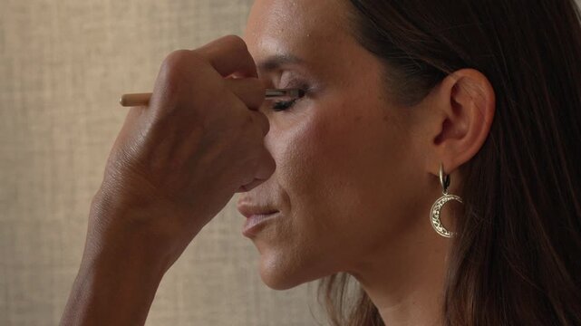 Makeup, woman, beauty, artist applying eyeshadow to eyelid close up in profile, cosmetic professional work