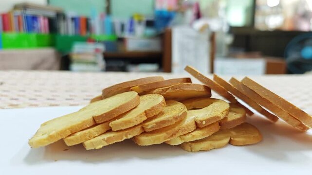 Heap of golden baked bread rusks on white foreground with blurred room background.