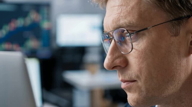 Male trader wearing glasses analyzing stock market charts on laptop, Bitcoin and Ethereum data reflected in lenses, cryptocurrency investment and financial analytics concept, 4K video