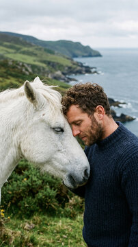 Man and white horse share a tender moment on a scenic coastal cliff