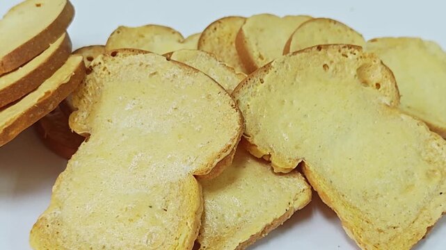 Close up of mini crispy toast rusks stacked on white surface.