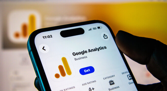 Closeup of a hand holding a smartphone displaying the google analytics app store page on a screen
