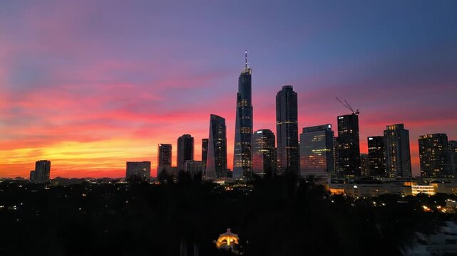 Modern Kuala Lumpur city skyline with Merdeka 118 tower framed by silhouetted palm trees during a colorful sunset