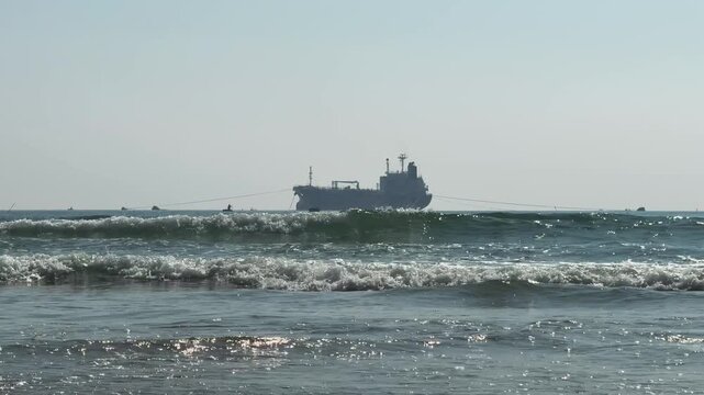 Silhouette of big Cargo ship on horizon. Low angle View from the beach with waves in the foreground