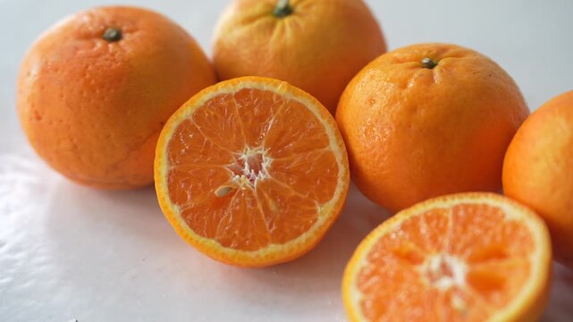 Fresh oranges arranged on a white surface, with halved fruits revealing their juicy segments. Oranges are widely used during Chinese New Year as auspicious fruits symbolizing prosperity, wealth, good 