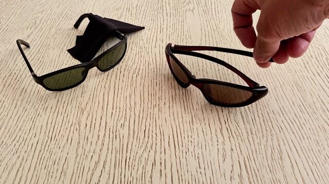 Two pairs of sunglasses placed on a light wooden tabletop. Stylish eyewear with tinted lenses displayed indoors, highlighting fashion accessories, everyday use, and modern style