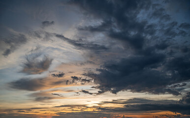 Fototapeta premium Dramatic Sunset Sky Background, Dark Storm Clouds Mixing with Golden Evening Light and Wispy Formations.
