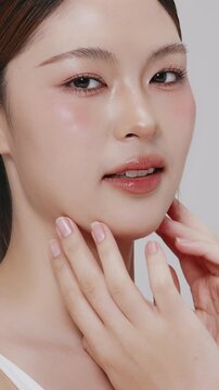 Vertical footage beautiful young Asian woman with healthy facial skin isolated over white background for skincare commercial product advertising. Slow motion shot.