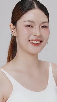 Vertical footage beautiful young Asian woman with healthy facial skin isolated over white background for skincare commercial product advertising. Slow motion shot.