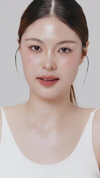 Vertical footage beautiful young Asian woman with healthy facial skin isolated over white background for skincare commercial product advertising. Slow motion shot.