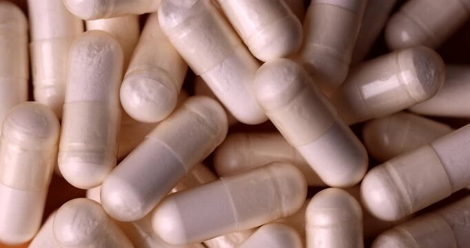 Overhead horizontal layout of transparent pharmacy pills rotating under a sharp direct beam of hard side light on a sleek surface